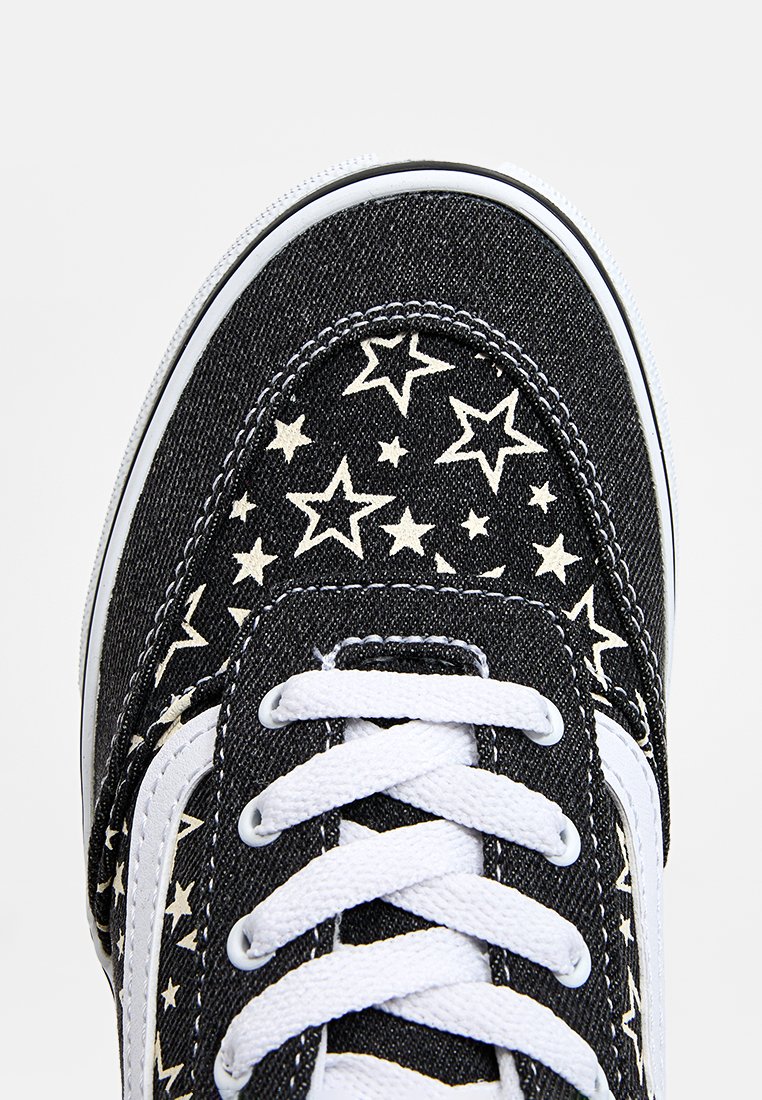 Zapatillas altas de lona negra con un patrón de estrellas blancas, cordones blancos y detalles en blanco. Cuenta con una puntera redonda y un collar acolchado.