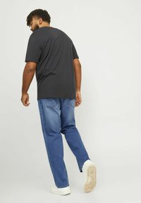 T-shirt nera a maniche corte, jeans in denim e sneakers bianche; il t-shirt ha una vestibilità comoda con scollatura rotonda. La texture appare liscia.