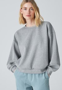 Felpa grigia oversized con spalle scese, polsini a costine e scollatura rotonda. Abbinata a pantaloni in corduroy blu chiaro.