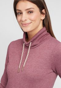 Cowl neck tröja i en melerad burgundyr�öd färg. Har dragsnören med guldfärgade ändar och en mjuk, texturerad yta.