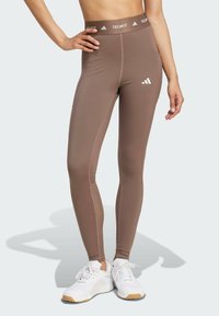 Hnědé sportovní legíny s vysokým pasem, s bílým brandingem "TECHFIT" a malým bílým logem, vyrobené z hladké, elastické látky.