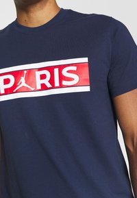Námorně modré bavlněné tričko s velkým červeným a bílým grafickým designem se slovem "PARIS" a logem Jumpman, kulatým výstřihem a krátkými rukávy.