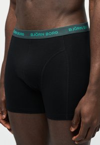 Ανδρικός κορμός που φοράει μαύρα μπόξερ με σκοτεινή πράσινη μέση όπου γράφει "BJÖRN BORG" με τουρκουάζ γράμματα.