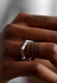 Silver ring with a textured surface and a rectangular shape, featuring a row of small, clear stones along the band. Skin tones visible.