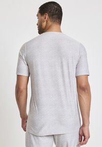 Szara koszulka z krótkim rękawem, wykonana z miękkiego, teksturowanego materiału, z klasycznym okrągłym dekoltem i luźnym krojem, który jest nieco dłuższy z tyłu.