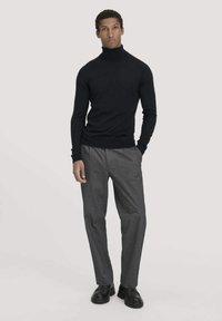 Schwarzer Rollkragenpullover aus glattem Material, kombiniert mit grauen, maßgeschneiderten Hosen. Texturierte Schuhe runden das Outfit ab. Einfaches Design, körpernahe Silhouette.