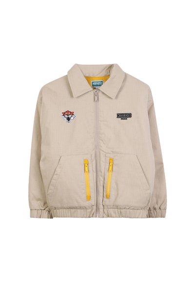 Veste zippée beige avec des poignets élastiques, deux poches zippées jaunes, logo Kenzo Paris sur la poitrine droite et patch de tête de tigre sur la poitrine gauche.