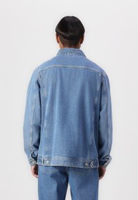 Denim jacket with a classic cut, light blue color, contrasting stitching, and snap closure accents. Features a standard collar and long sleeves.