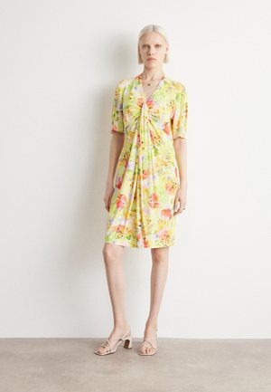 Blumenkleid mit gelbem Grund und pinken sowie grünen Blumen, kurzen Ärmeln und einem gerafften Vorderteil. Kombiniert mit beigen Riemchenheels.