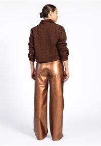 Bruine gestructureerde jacket met een kraag, gecombineerd met glanzende, hooggewaisted, wijde koperen broeken. De achteraanzicht toont de pasvorm en stofdetails.