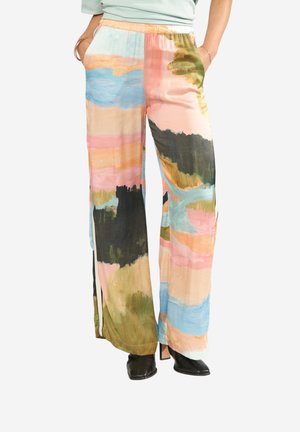 Volné široké kalhoty s barevným abstraktním vzorem tahů štětcem v pastelových a tmavých tónech, nošené s černými kotníkovými botami.