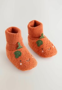 Bottines tricotées orange avec un poignet côtelé, ornées de broderies de feuilles vertes et de visages souriants. Texture douce avec un design confortable.