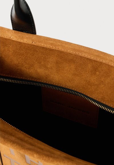 Barna velúr táska belső része fekete cipzárral, rajta egy bőr címke, amelyen az áll, hogy "MARC JACOBS". Simább textúrával és strukturált dizájnnal rendelkezik.