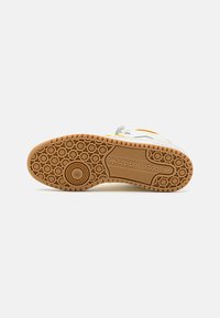White sneaker sole with a patterned gum rubber outsole, featuring circular grips and an embossed brand logo. Accents include yellow stripes.