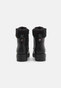 Bottines en cuir noir avec un revers en fourrure noire, un intérieur texturé et un petit talon bloc. Présente un accent décoratif sur le côté.