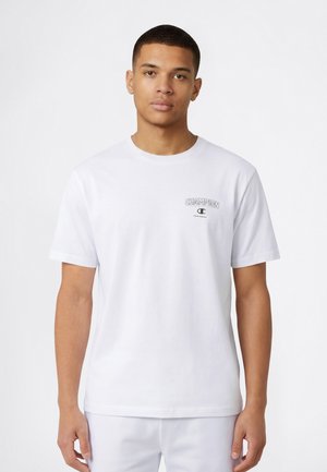 Maglietta bianca in cotone con maniche corte e scollo rotondo, con un piccolo logo nero "Champion" sul petto a sinistra. Tessuto liscio.