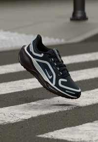 Dark blue athletic shoe with gray accents, lightweight mesh upper, prominent Nike swoosh, and textured rubber sole, suspended above a crosswalk.