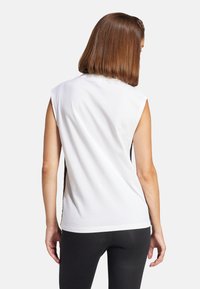 Top blanco sin mangas con un escote redondeado, que presenta paneles laterales negros y una textura de algodón suave, combinado con leggings negros.