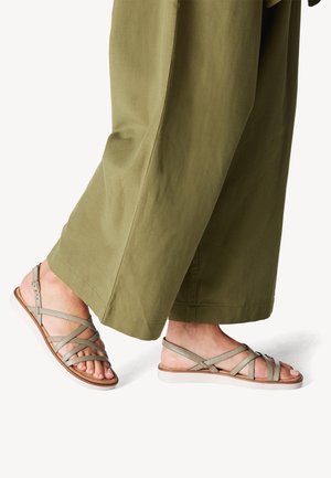 Grau gestrickte Sandalen mit Riemchen im Kreuzdesign, flacher Sohle und verstellbarem Knöchelriemen, kombiniert mit lockeren olivgrünen Hosen.