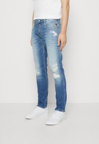 Tajta jeans i ljusblå denim med urtvättade accenter och slitna lappar. Har klassisk femficksdesign och dragkedja. Matcher med vita sneakers.