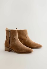 Cizme scurte maro din piele intoarsă, cu vârfuri ascuțite, fermoare laterale și cusături decorative. Tocuri joase din lemn completează designul.