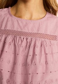 Roze, geborduurde blouse met een ronde halslijn, voorzien van bloempatronen en kant uitsparingen op de borst en gatherstof bij de taille.