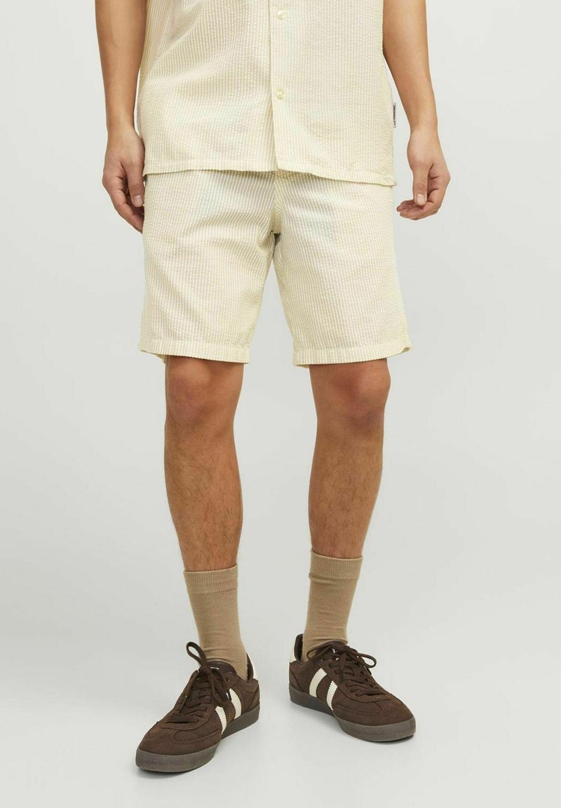 Pantalones cortos de rayas amarillas claras hechos de una tela suave, con corte recto y dobladillos enrollados, combinados con zapatillas marrones y calcetines beige.