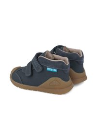 Zapatitos de niño pequeños en azul marino con suelas de goma marrón, dos tiras de Velcro y etiqueta de tela BIO tex en el costado.