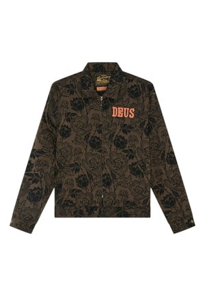 Persona con una chaqueta marrón con estampado floral encima de una sudadera amarilla con gráfico y shorts vaqueros grises descoloridos con bordes deshilachados.