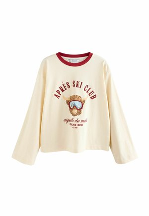 Cream long-sleeve t-shirt featuring a red crew neck, graphic of a mountain goat wearing goggles, and "APRÉS SKI CLUB" text in maroon.