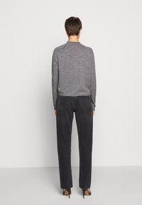 Grauer, langärmeliger Pullover mit rundem Ausschnitt, kombiniert mit hoch taillierten, weit geschnittenen schwarzen Jeans. Schwarze Absatzschuhe vervollständigen den Look.