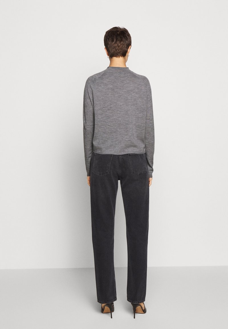 Grauer, langärmeliger Pullover mit rundem Ausschnitt, kombiniert mit hoch taillierten, weit geschnittenen schwarzen Jeans. Schwarze Absatzschuhe vervollständigen den Look.