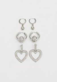 Drie paar zilveren oorbellen: twee kleine hoops met een druppelparel en een paar met hartvormen bezaaid met rhinestones.