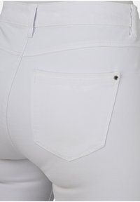 Weiße Denim-Jeans mit taillierter Passform. Verfügt über eine Gesäßtasche mit einem Diamantdesign und einem Metallnieten. Glatte Textur und saubere Nähte.