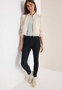 Beige cropped bomberjack, lichtgrijs shirt, zwarte slimfit broek en beige sneakers. Soepele stof en elastische manchetten. Eenvoudige stijl.