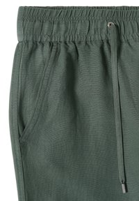 Gros plan sur un pantalon à taille élastique verte avec poche latérale et cordon de serrage à embout métallique.