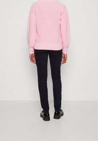 Maglione a maglia rosa oversize con polsini e orlo a coste, abbinato a pantaloni slim-fit blu scuro e scarpe nere resistenti.