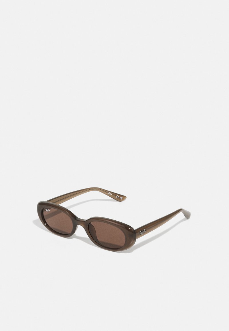 Braune ovale Sonnenbrillen mit dunklen Gläsern. Das Gestell besteht aus einem transparenten braunen Material und hat ein auf den Bügeln aufgedrucktes Logo.
