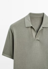 Polo vert clair à manches courtes en tissu texturé avec un col, visible de la partie supérieure de la poitrine jusqu'à la zone des épaules.