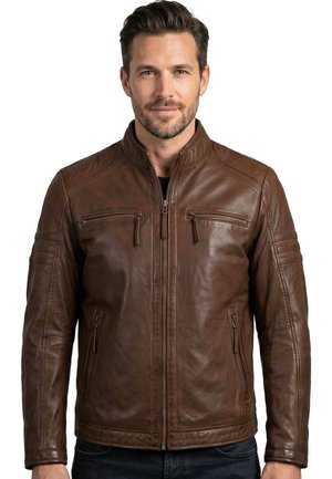 Mann trägt eine dunkelbraune Lederjacke mit Reißverschlusstaschen an Brust und Seiten und steht vor weißem Hintergrund.