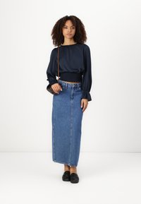 Mornarska bluzica s pufastimi rokavi, skrajšan dizajn; modri denimski maxi krilo; črne loafers čevlje; preprosta torbica preko telesa. Gladek material in klasičen kroj.