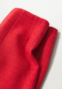 Tissu rouge texturé plié avec des coutures visibles et une surface légèrement rugueuse tissée sur un fond blanc.