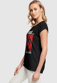 Juodas medvilnės marškinėliai su grafine Deadpool atvaizdu. Trumpomis rankovėmis, laisvas kirpimas ir ryškus tekstas balta ir raudona spalvomis.