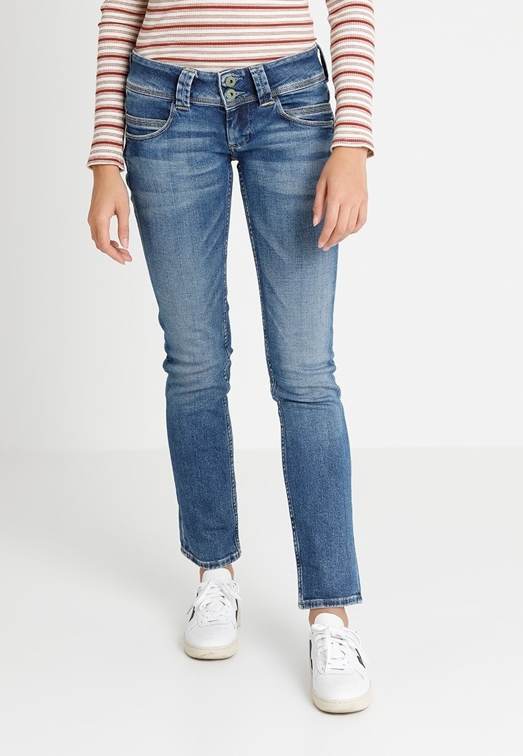 Světlé modré džíny s úzkým střihem, pěti kapsami, jemným vyblednutím a uzávěrem na dva knoflíky. V kombinaci s bílými sportovními botami.