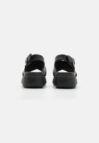 Svart lærsandaler med justerbar spenne, åpen bakside og chunky svart såle. Glatt tekstur og enkelt design.
