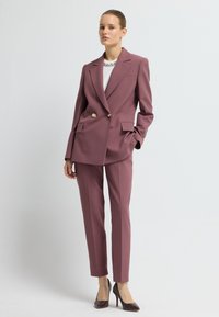 Tweedelig pak in mauve, met een dubbelzijdige blazer met gouden knopen en op maat gemaakte broek. Gladde stof met een gestructureerde pasvorm.