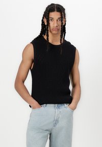 Black, sleeveless knitted tank top with a textured diamond pattern. Paired with light blue denim jeans, featuring a relaxed fit.