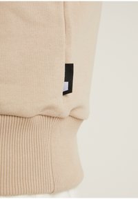 Tessuto lavorato a maglia beige con vita a costine e un piccolo etichetta rettangolare nera e bianca cucita nella cucitura laterale.