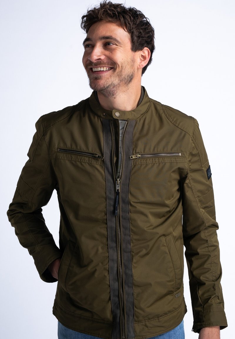 Giacca bomber verde oliva con zip frontale, due tasche sul petto e colletto rialzato; presenta un tessuto testurizzato e dettagli a contrasto.