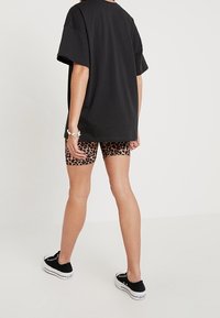 Camiseta negra de gran tamaño, pantalones cortos de ciclismo con estampado de leopardo y zapatillas negras combinados; estilo casual con patrones y texturas contrastantes.